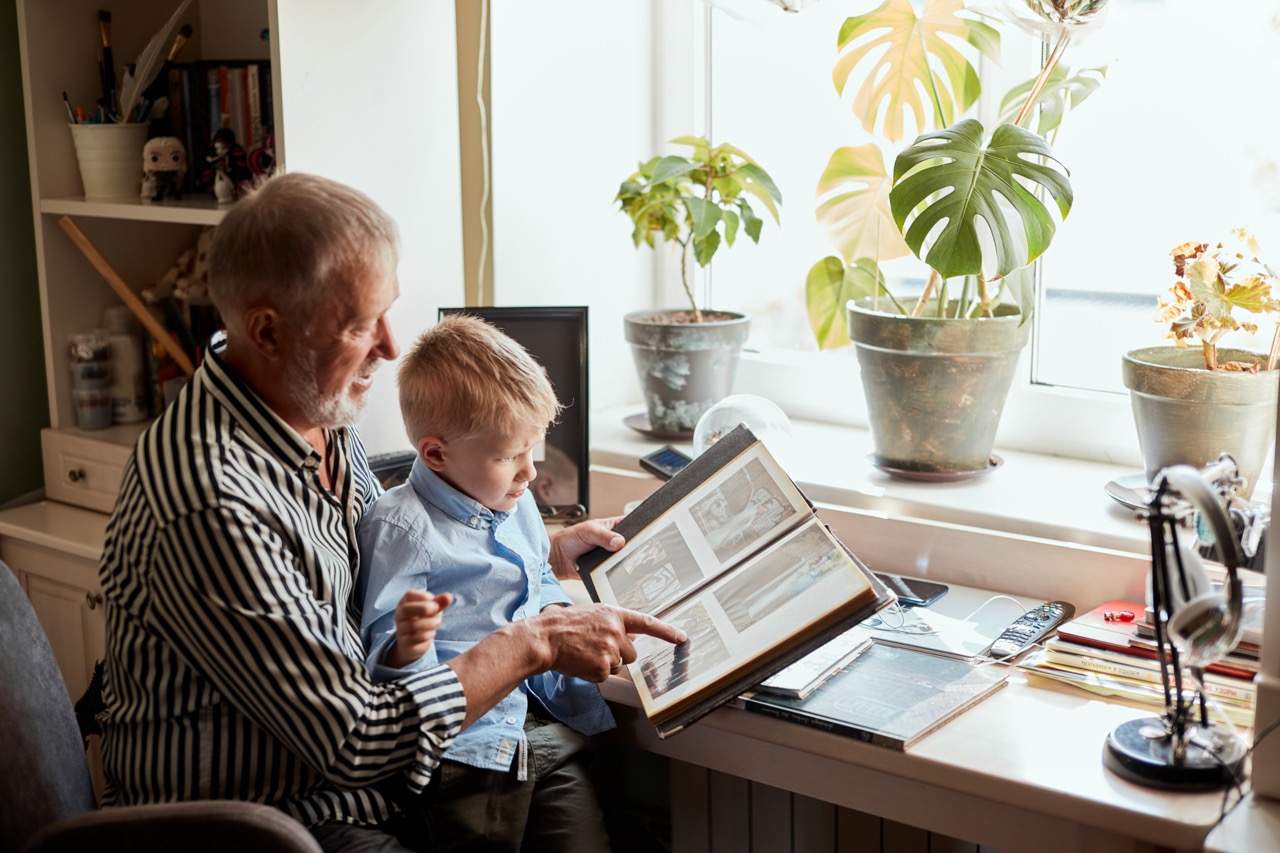 Grandfather and grandson on sofa at home. Grandpa and children looking at old photos